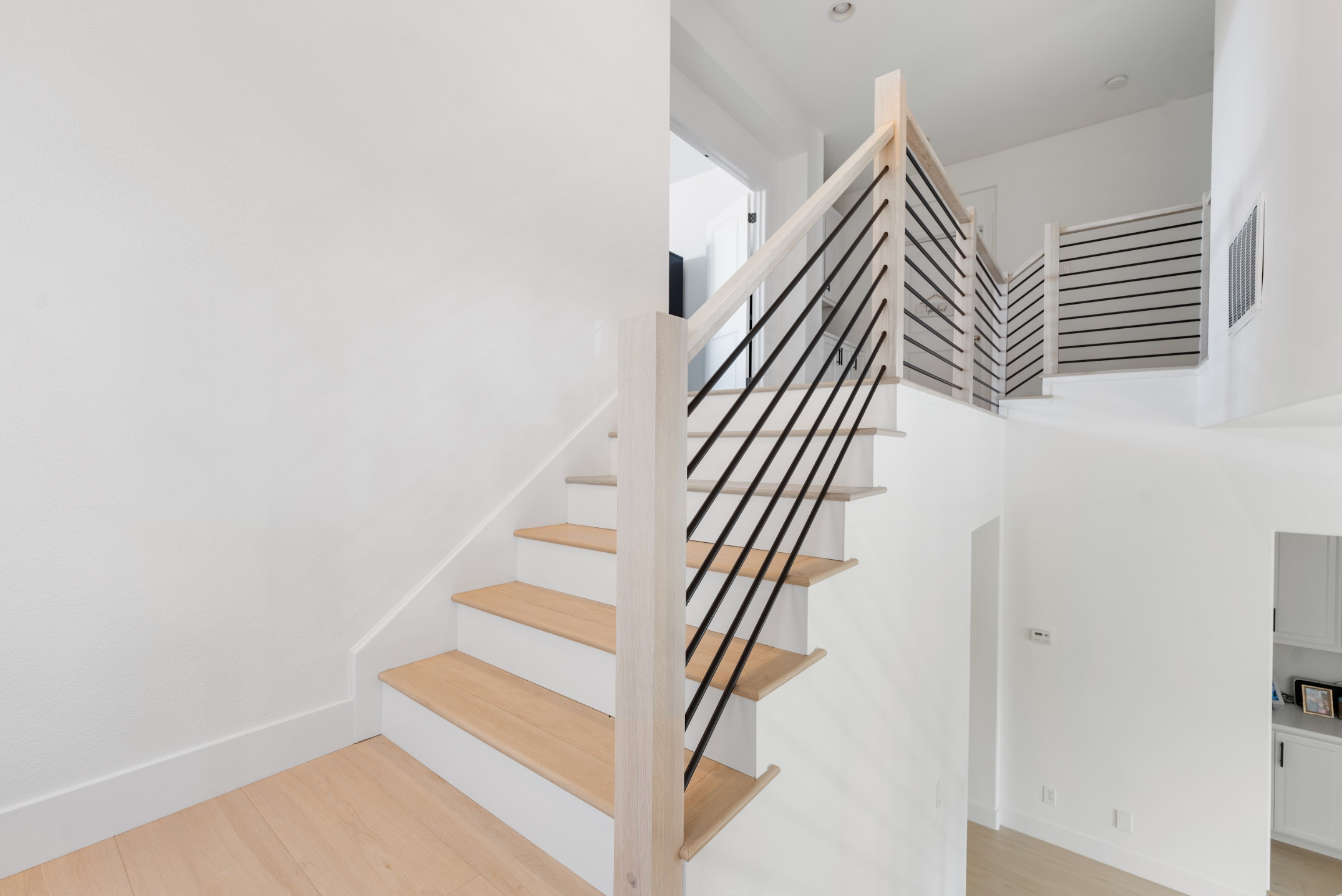 Modern staircase with wooden steps and black horizontal balusters, wood railings in a white interior.